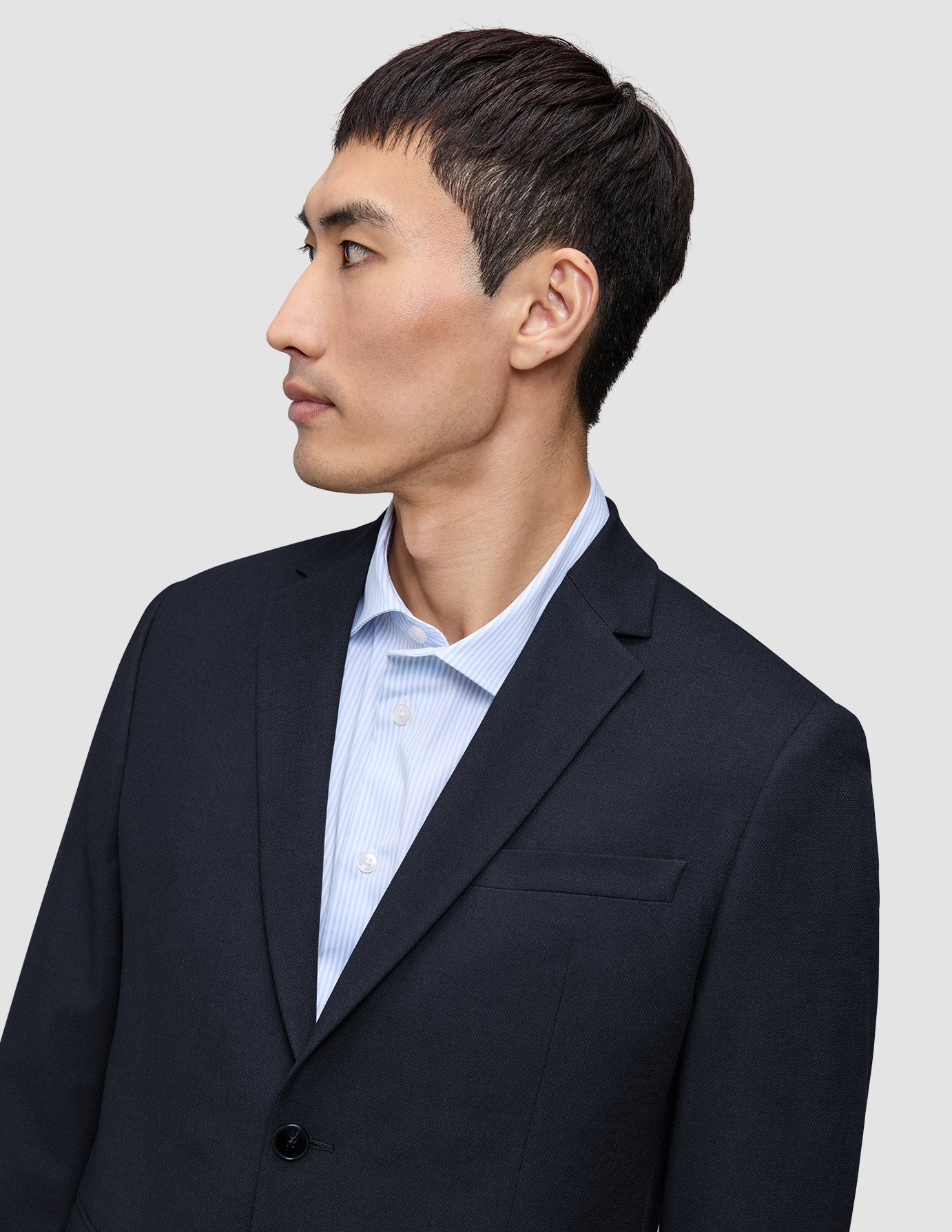 Eine Person im Profil, von der Brust aufwärts, die einen Motion Blazer Regular in Mitternachtsblau über einem hellblau gestreiften Hemd trägt.